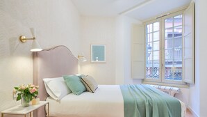 A bedroom with a bed, bedside table, lamp, window, and a view of the outside. - Charming 2-Bedroom Apartment in Central Malaga with Modern Amenities (Málaga)