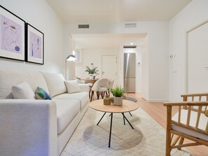 Una sala de estar moderna con un sofá, una mesa de centro y sillas. Hay una zona de comedor con una mesa y sillas, y una cocina con un refrigerador.
