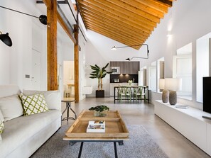 Un salon moderne avec un plafond en bois, un canapé, une table basse et une cuisine en arrière-plan.