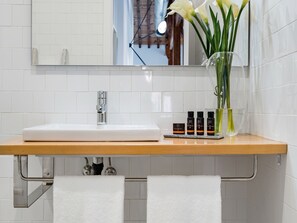 Une salle de bain avec un lavabo blanc, un miroir, un porte-serviettes et un vase avec des fleurs.