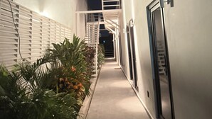 Un couloir étroit et bien éclairé, avec une façade blanche, un escalier en métal et une porte sur le côté droit.