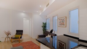 Un salon moderne avec un canapé, un fauteuil, une petite table sur laquelle est posé un vase, et un lave-linge dans un coin.