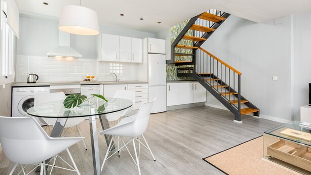 Een moderne keuken met witte kasten, een glazen eettafel en een houten trap.