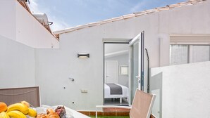 Een klein buitenhoekje met een gedekte tafel, een stoel en uitzicht op een slaapkamer door een open deur.