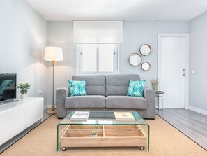 Ein modernes Wohnzimmer mit einem grauen Sofa, einem Glastisch und einem Fernseher auf einem weißen Schrank.