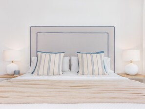 Ein ordentlich bezogenes Bett mit Kopfteil, zwei Nachttischlampen und einer flauschigen, beige farbenen Decke.