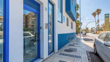 Un edificio con fachada azul y blanca, una entrada visible con puerta azul y una acera pavimentada.