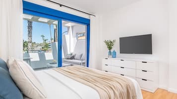 Een moderne slaapkamer met een bed, een televisie en een balkon met uitzicht op palmbomen.