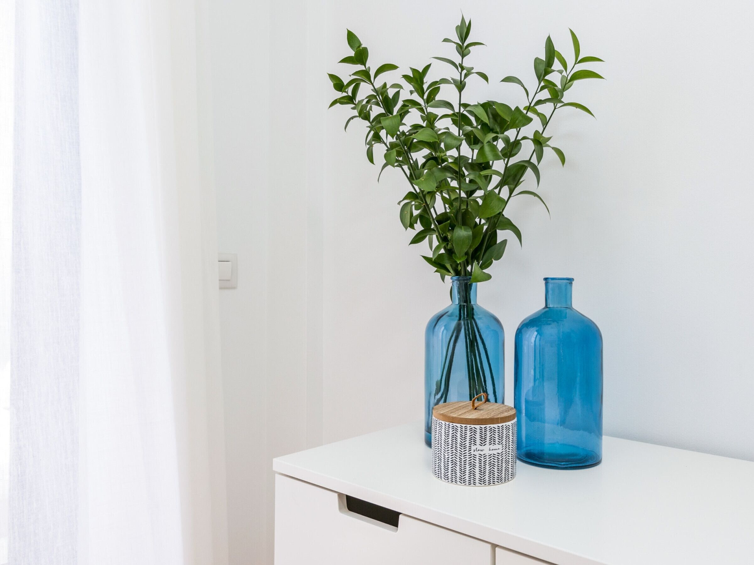 Un mueble blanco con dos jarrones azules de vidrio y un pequeño recipiente estampado encima.