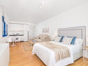 Ein modernes, helles Schlafzimmer mit einem großen Bett, Nachttischen und Blick auf eine Küche und ein Wohnbereich.