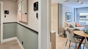 Et hotellobby med et moderne design, inklusive et siddeområde med et rundt bord og stole, en sofa og et stort abstrakt maleri på væggen.