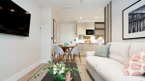 En moderne stue med sofa, sofabord med blomsterarrangement, spiseområde med stole og et køkken i baggrunden.