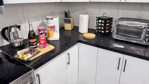 Ett modernt kök med vita skåp, en svart bänkskiva, en kaffemaskin från Keurig, en brödrost och diverse köksredskap.