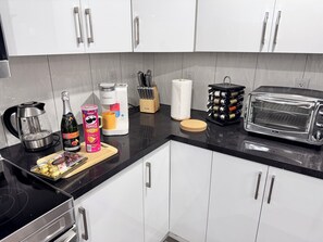 Eine moderne Küche mit weißen Schränken, einer schwarzen Arbeitsplatte, einer Keurig-Kaffeemaschine, einem Toaster und verschiedenen Küchenutensilien.