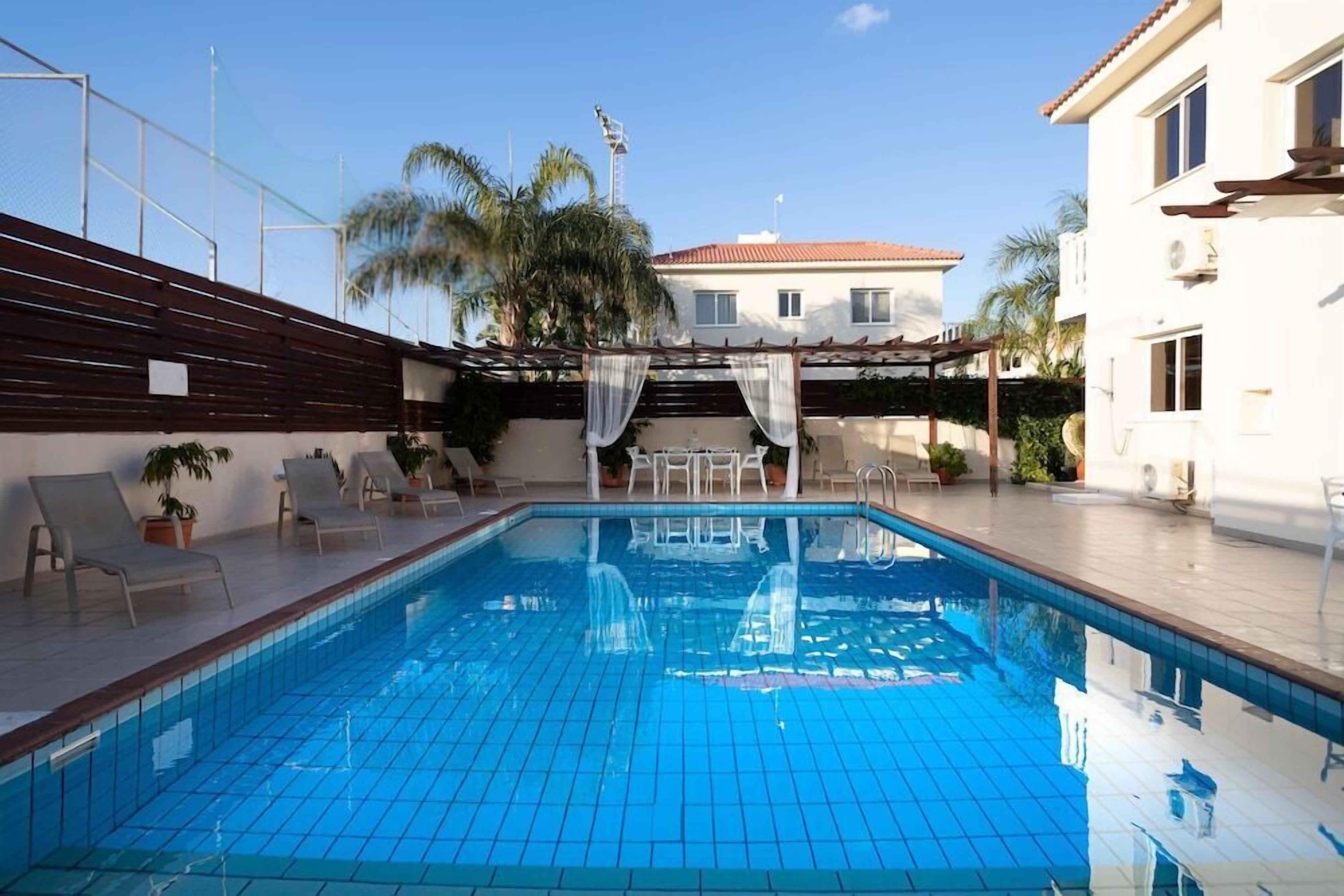 A swimming pool with tiled flooring, surrounded by lounge chairs and potted plants.