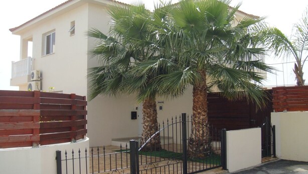 A two-story house with a white exterior, a red roof, and a black metal gate. - Athena Villa (Ayia Napa)