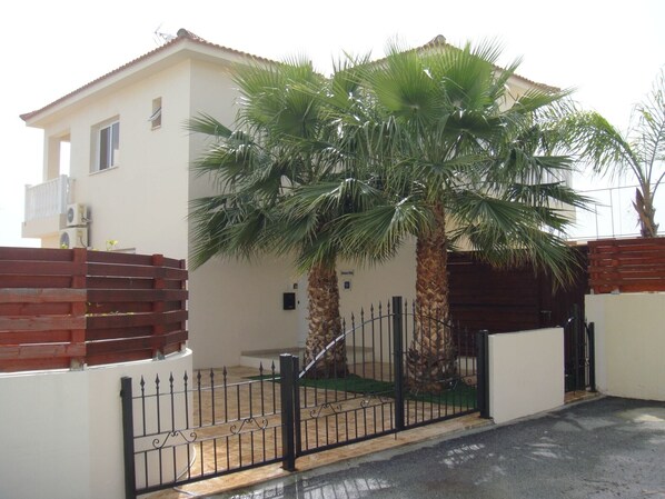 A two-story house with a white exterior, a red roof, and a black metal gate. - Athena Villa (Ayia Napa)