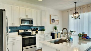 Una cucina moderna con mobili bianchi, elettrodomestici in acciaio inossidabile, una parete backsplash blu e un'isola centrale con un lavello.