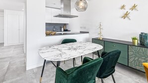 Eine moderne Küche mit einem Marmortisch, grünen Stühlen und einer Pendelleuchte.