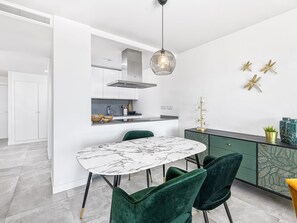 Eine moderne Küche mit einem Marmortisch, grünen Stühlen und einer Pendelleuchte.