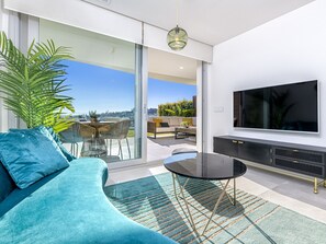 A modern living room with a curved teal sofa, a glass sliding door leading to a balcony, a flat-screen TV, and a small round table. - Elegantly furnished apartment with pool, jacuzzi, spa, and garden in Fuengirola (Fuengirola)