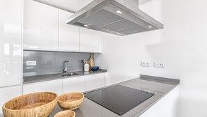 Eine moderne Küche mit weißen Schränken, einer schwarzen Induktionskochplatte und Holzkielen auf der Arbeitsfläche.