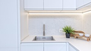 A modern kitchen with white cabinetry, a stainless steel sink, a marble backsplash, and a small potted plant on the countertop. - Bright apartment in Málaga (Málaga)