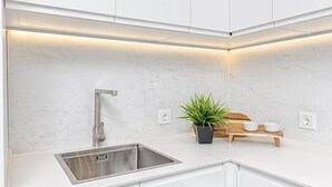 A modern kitchen with white cabinets, a stainless steel sink, a potted plant, and a wooden sideboard with bowls. - Bright apartment in Málaga (Málaga)