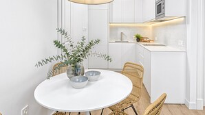 A modern kitchen with white cabinetry, a round dining table with wicker chairs, and a hanging light fixture. - Bright apartment in Málaga (Málaga)