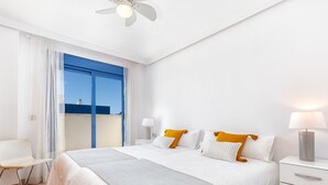 Ein modernes Hotelzimmer mit einem großen Bett, einem Nachttisch mit Lampe, einem Sessel und Blick auf den Himmel durch ein Fenster.