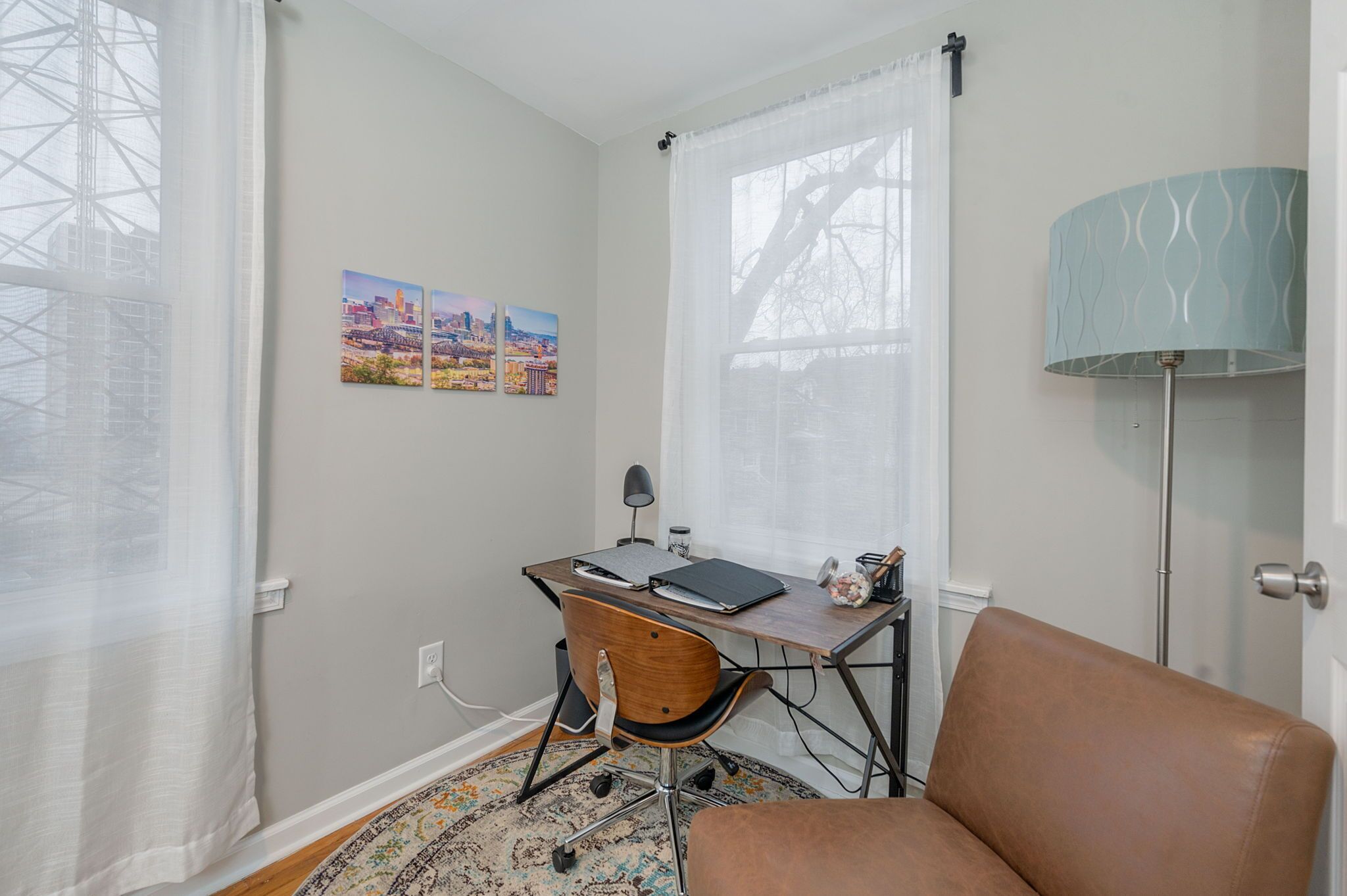 A room with a desk, chair, lamp, and artwork on the wall.