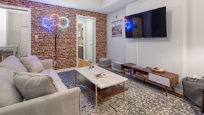 Un salon moderne avec un mur en briques, un téléviseur à écran plat, un canapé, une table basse et une petite table d’appoint.