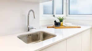 Een moderne keuken met een roestvrijstalen spoelbak, witte kastjes en een raam met geëtste glas.