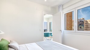 Een slaapkamer met een bed, een raam met uitzicht op gebouwen en een deur naar een andere kamer.