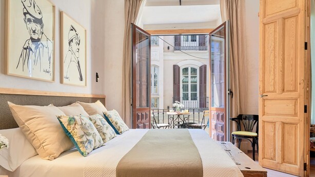 Ein Schlafzimmer mit einem großen Bett, einem Holz-Kopfteil und Blick auf einen Balkon mit Gartenmöbeln.