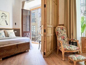 A bedroom with a bed, a wooden chair with floral upholstery, and a wooden bench. - Elegant Apartment with Balcony in the Heart of Malaga, Modern Amenities, Sleeps 5 (Málaga)