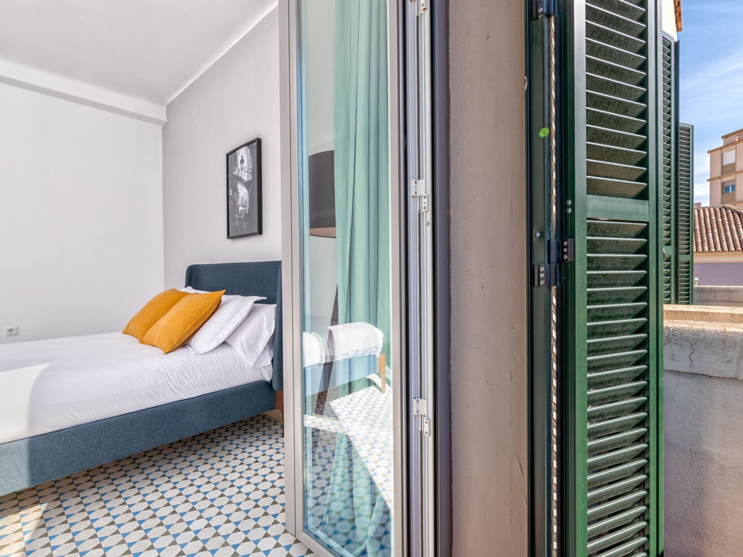 Een slaapkamer met een bed, een inlijsting foto aan de muur en een raam met groene luiken.
