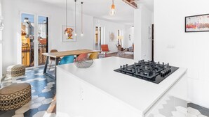Eine moderne Küche mit einer zentralen Kochinsel, einem Essbereich mit Holztisch und Stühlen und Blick auf die Stadt durch große Fenster.