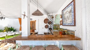Una cocina con una isla central, taburetes de bar, ollas colgantes y un salpicadero de azulejos.