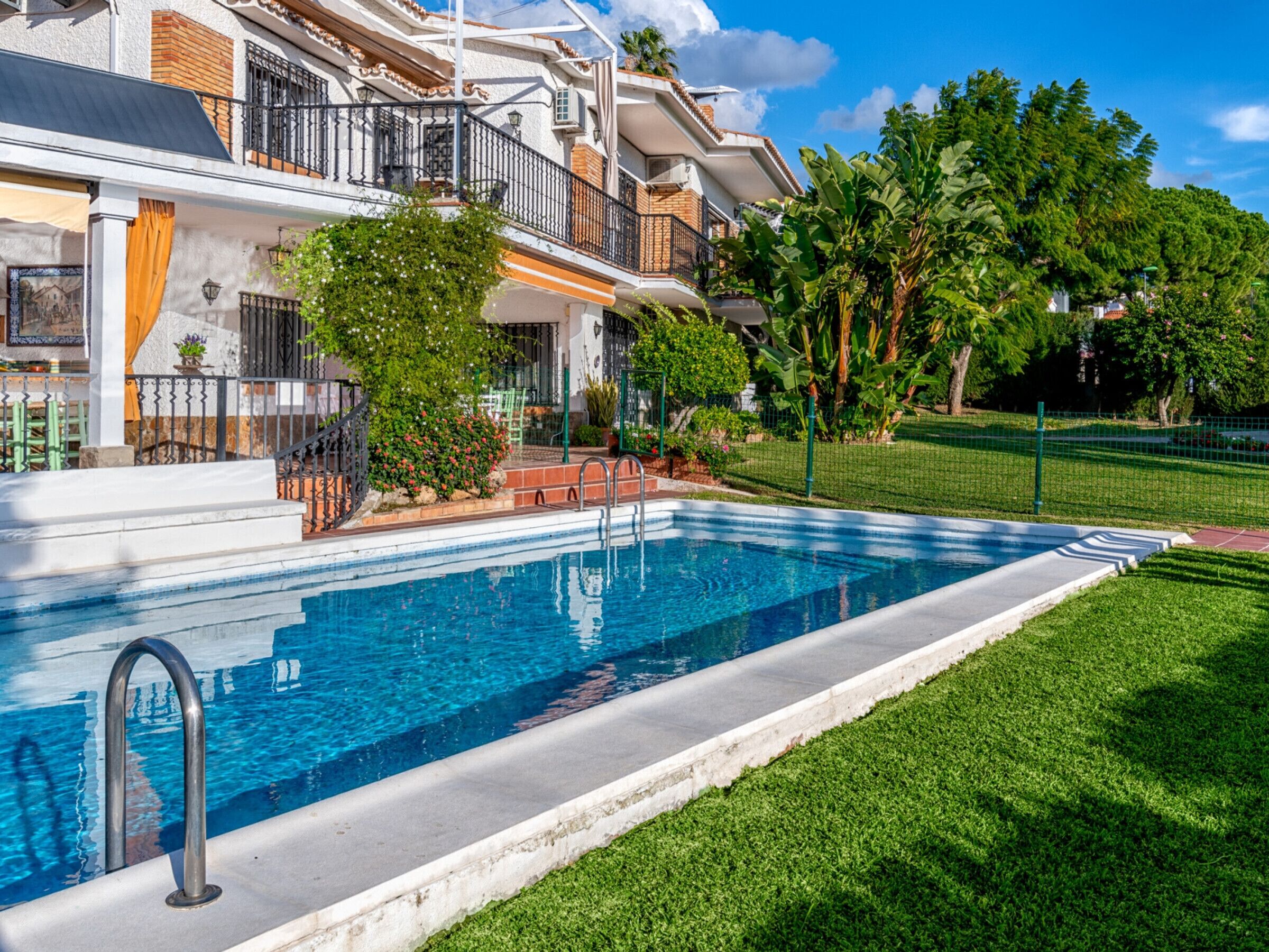 A swimming pool with a clear blue water, surrounded by a well-maintained lawn and a house with a balcony.