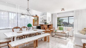 Amplia sala de estar con una mesa de comedor, bancos y una mesa de centro. Hay una chimenea, un sofá y un ventanal con vistas al exterior.