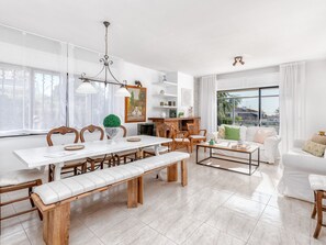 A spacious living area with a dining table, benches, and a coffee table. There is a fireplace, a sofa, and a large window providing a view outside. - Luxury villa with pool and garden, 1km from beach - sleeps 12 (Málaga)