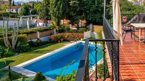 Una piscina rodeada de exuberante vegetación, un patio con mobiliario exterior y vistas del barrio.