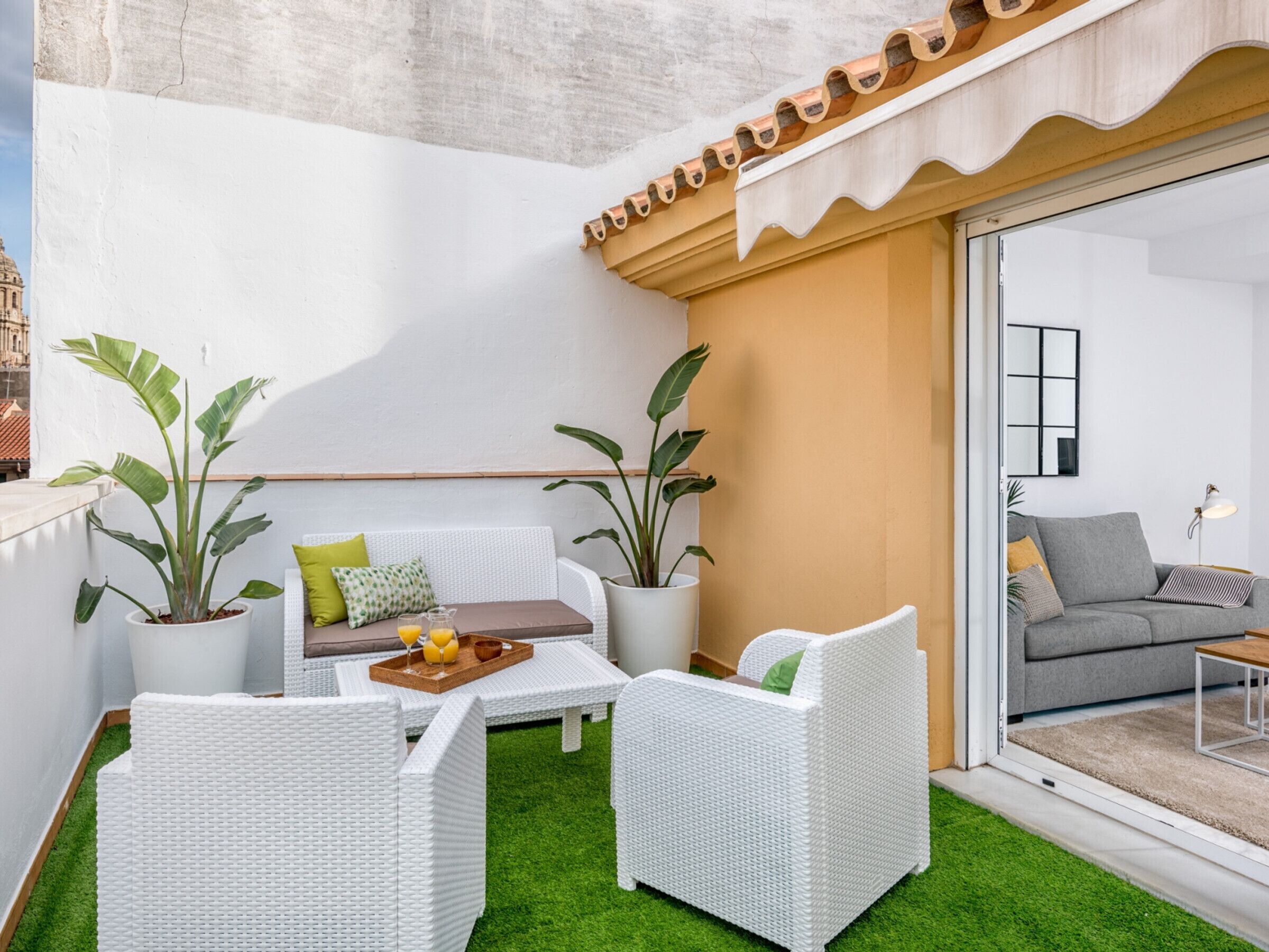 A balcony with white wicker furniture, green artificial grass, and potted plants.