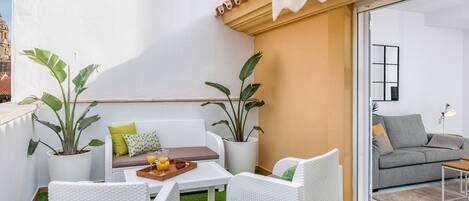 A balcony with white wicker furniture, green artificial grass, and potted plants.