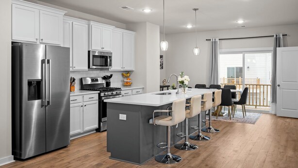 Una cocina moderna con armarios blancos, electrodomésticos de acero inoxidable, una isla central con taburetes y un comedor con vistas al exterior.