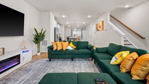 Una sala de estar moderna con un sofá verde, un televisor de pantalla plana, una chimenea y una escalera.