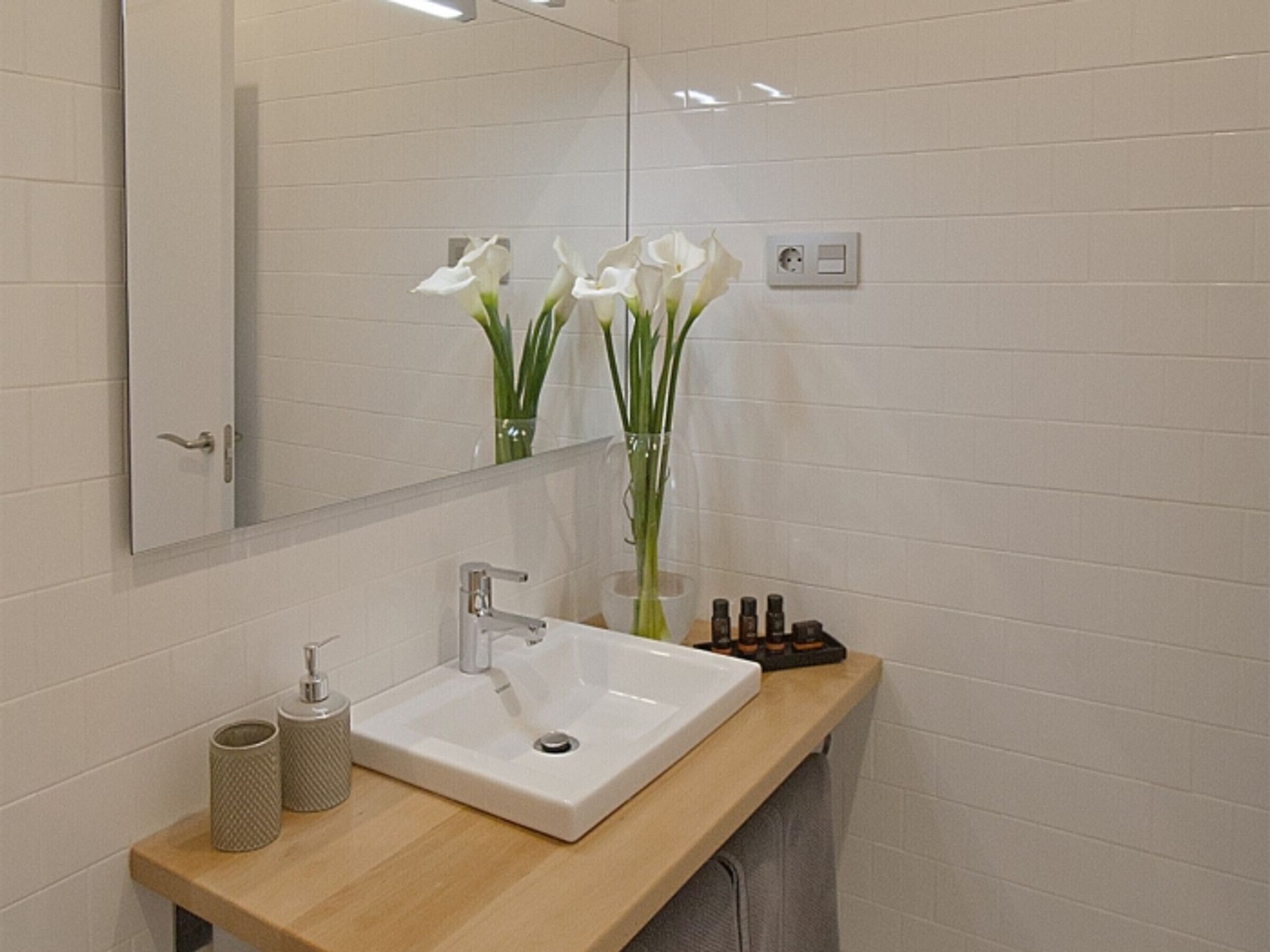 A modern bathroom with a white sink, a mirror, and a vase with white flowers.