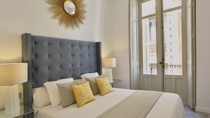 Ein Schlafzimmer mit einer gepolsterten Kopfteile, zwei Nachttischlampen, einem großen Spiegel und Blick durch eine Tür nach draußen.