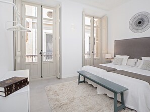 A bedroom with a large bed, a bench, a bedside table, and a wall-mounted fan. - Elegant 2-bedroom apartment in Malaga center, air conditioning, WiFi, minimalist kitchen (Málaga)